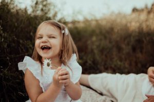Little girl laughing and holding a daisy