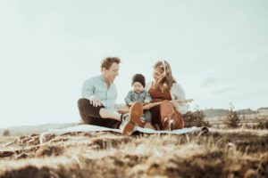 Parents and child playing guitar In the grass