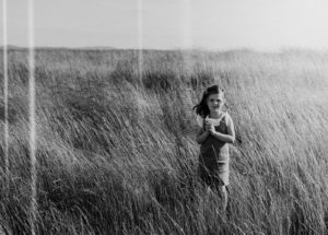 Girl in field of tall grass holding daisies