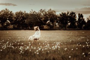 Little girl in white dress walking through daisy field