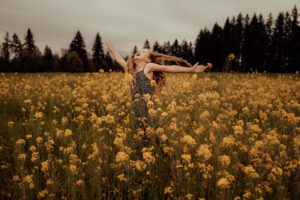 Curly haired girl jumping and laughing in a field of yellow flowers